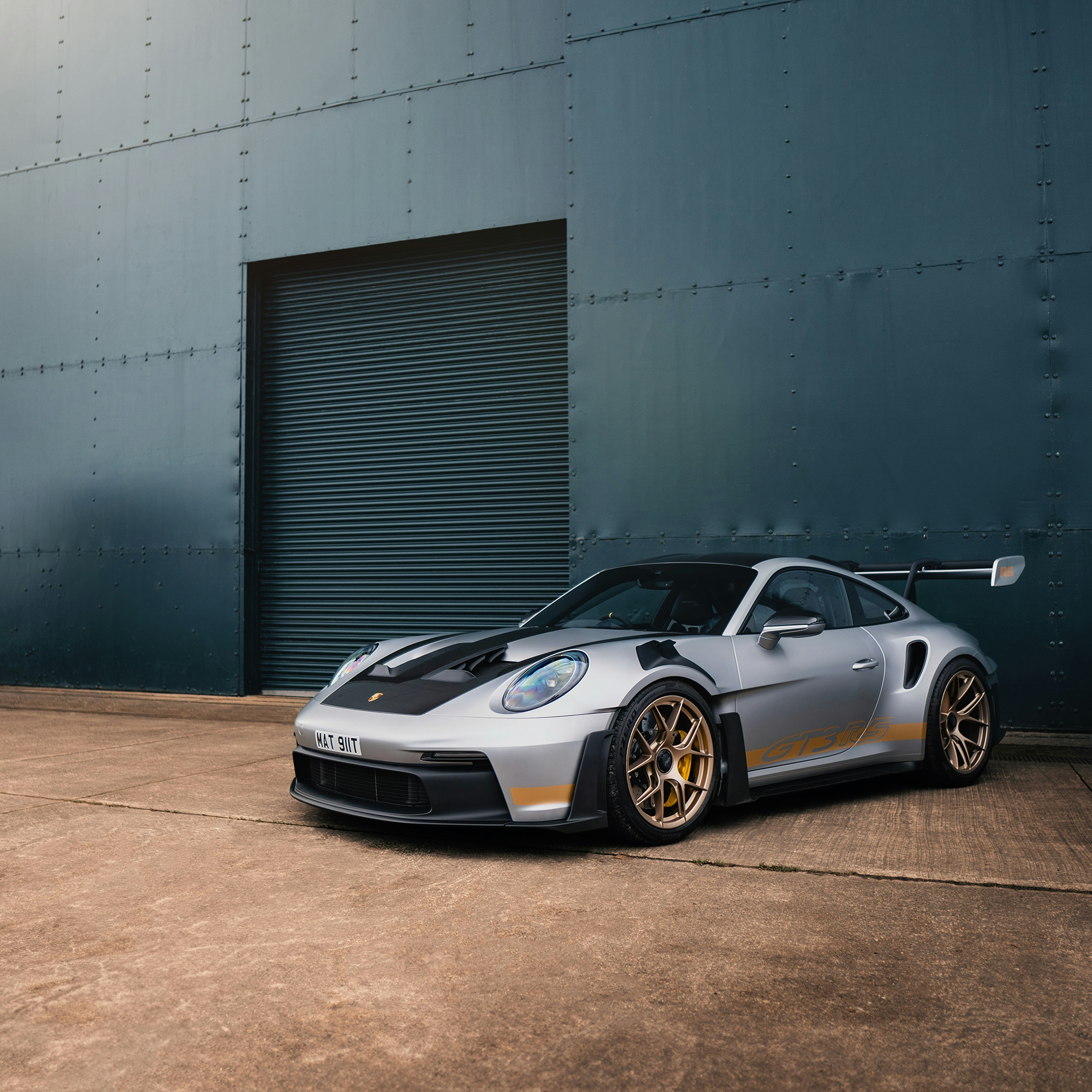 a side photo of a grey modified porsche 911 being in front of some sort of big warehouse building